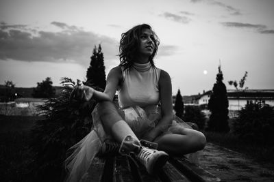 Young woman smoking while sitting on bench against sky