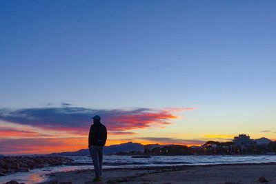 Rear view of silhouette man standing on beach during sunset