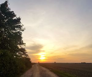 Road amidst trees against sky during sunset