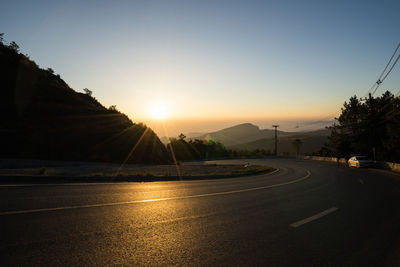 Road by city against sky during sunset