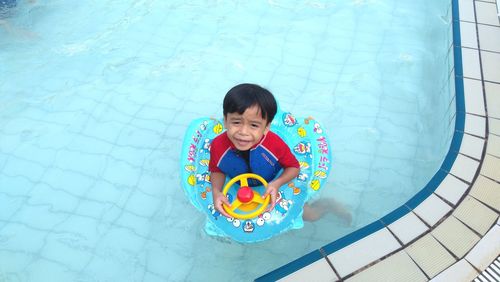 High angle view of happy boy playing with toy in swimming pool