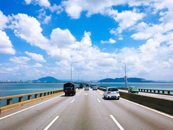 Cars on road by sea against sky