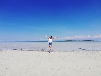 Rear view of woman standing at beach against blue sky