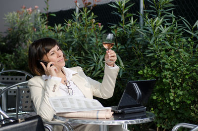 Businesswoman holding wineglass while talking on mobile phone