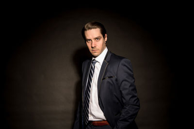 Portrait of confident businessman standing against black background