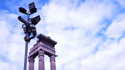 Low angle view of flood light and historic columns against cloudy sky