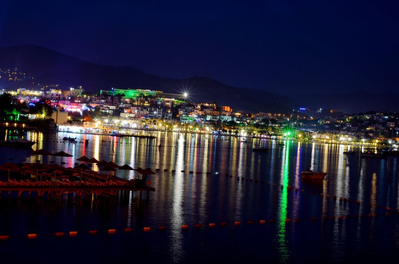 illuminated, night, water, reflection, architecture, built structure, waterfront, building exterior, mountain, river, clear sky, sea, city, lake, copy space, scenics, sky, tranquil scene, cityscape, mountain range