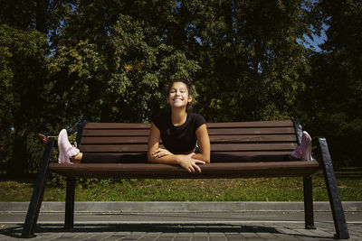 Girl in sportswear on a sunny summer day on the embankment in the park doing fitness and stretching