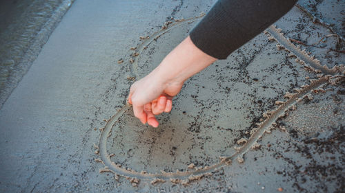 High angle view of hand drawing heart shape on wet sand at beach