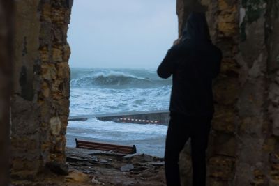 Man standing on rock by sea against sky