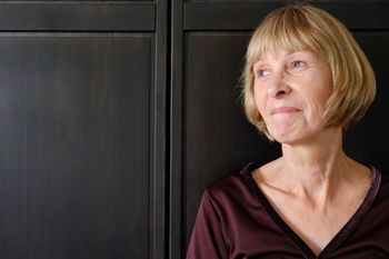 Mature woman looking away while standing against cabinet at home