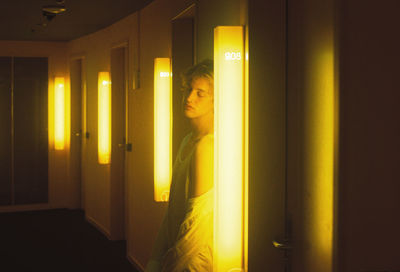 Portrait of young woman standing against illuminated window