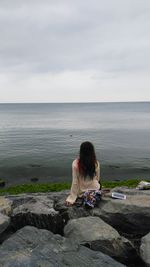 Rear view of woman sitting on rock against sea
