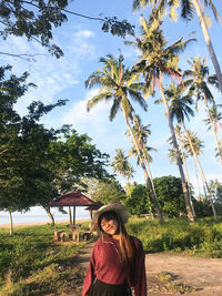 Portrait of woman standing by palm trees against sky