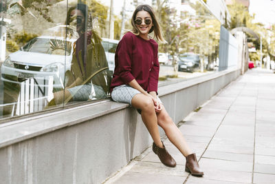 Full length of fashionable young woman sitting on footpath in city