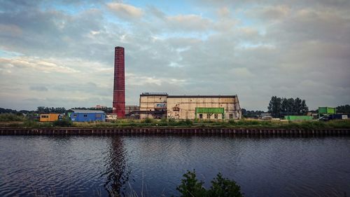River by abandoned factory against cloudy sky