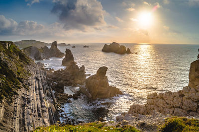 Rocks in sea against sky during sunset