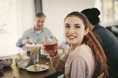 Smiling girl having drink while sitting with family at table during party