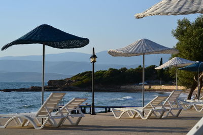 Deck chairs and parasols on beach against sky