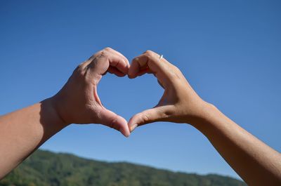 Low angle view of couple making heart shape against clear blue sky