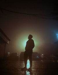 Rear view of silhouette man standing on illuminated street at night