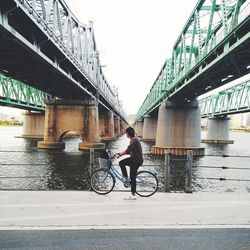 Man riding bicycle on bridge over river in city