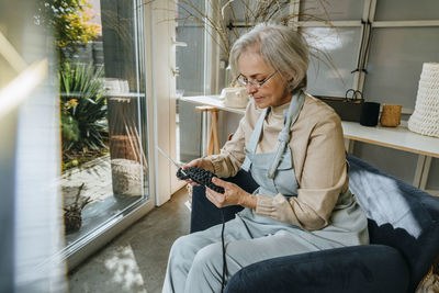 Craftswoman crocheting on armchair in workshop