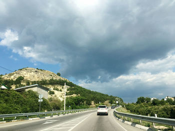 Cars on road against cloudy sky