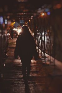 Rear view of woman walking on illuminated road in city at night