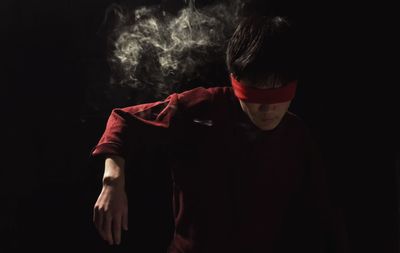 Smoke behind blindfolded man standing against black background