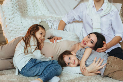 Pregnant mother with kids lying on bed at home