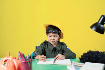 Portrait of boy sitting on table against yellow wall