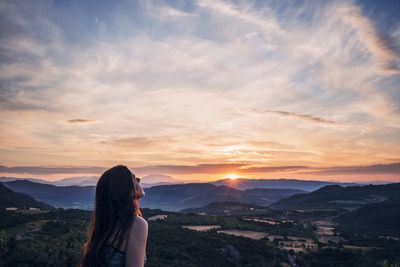 Young woman standing on mountain against sky during sunset