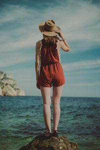 Rear view of woman standing on rock against sky