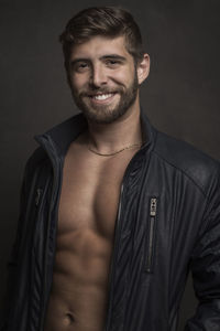 Portrait of smiling young man wearing leather jacket against black background