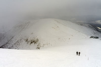 People by snowcapped mountain against sky