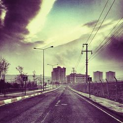 Road passing through city against cloudy sky