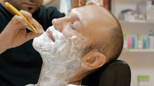 Midsection of barber doing shaving of mature man in salon