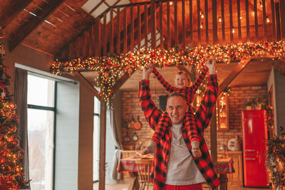 Candid authentic happy dad and son in red plaid pajamas fooling around at wood lodge xmas decorated