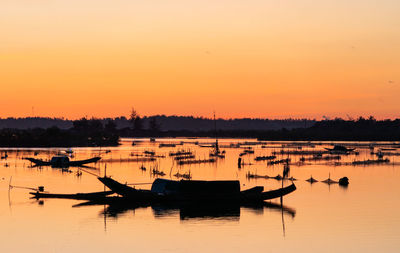 Silhouette boats moored in lake against orange sky