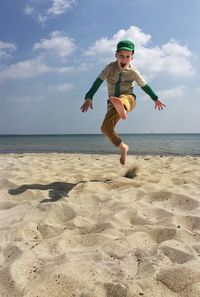 Boy jumping on beach against sky