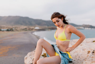 Woman sitting on rock against sky