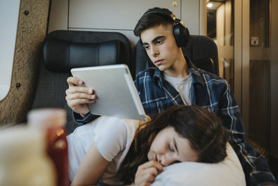 Boy watching tablet pc with sister sleeping on lap in train