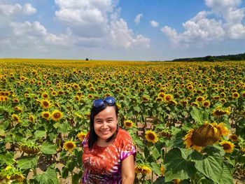 Portrait of girl on sunflower field against cloudy sky