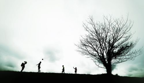 Silhouette people on bare tree against sky