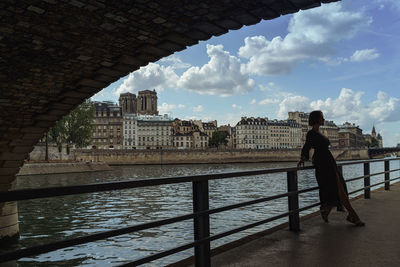 Woman standing on bridge over river against sky in city