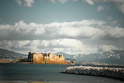 Buildings by sea against cloudy sky