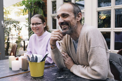 Happy father with hand on chin sitting by daughter on dining table at restaurant