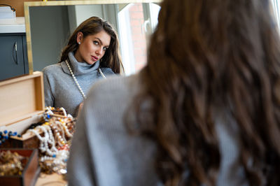 Reflection of a woman in mirror choosing and trying different jewelry, soft focus, close-up