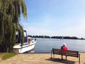 Rear view of man sitting on bench by sea against sky